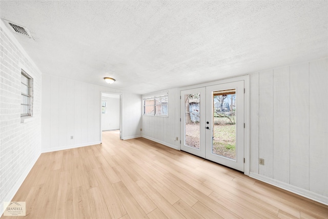 4725 Bruce St, Bossier City, LA 71111 - spare room with french doors, brick wall, a textured ceiling, and light hardwood / wood-style flooring