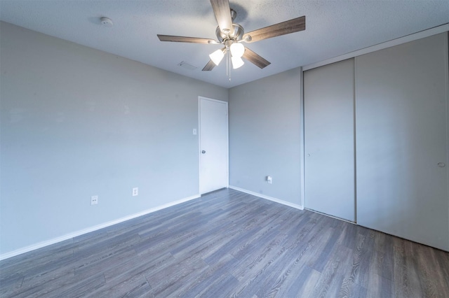 unfurnished bedroom featuring dark wood-type flooring, ceiling fan, a closet, and a textured ceiling