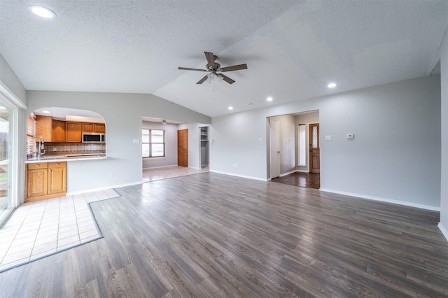 unfurnished living room featuring dark wood-type flooring, ceiling fan, vaulted ceiling, and a textured ceiling