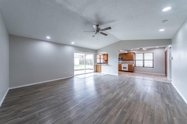 unfurnished living room featuring a healthy amount of sunlight, vaulted ceiling, dark wood-type flooring, and ceiling fan