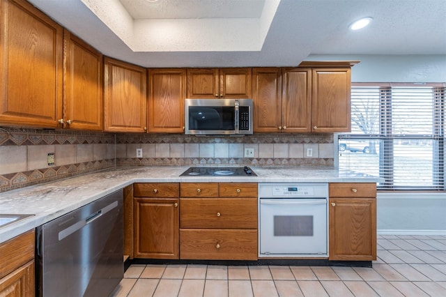 kitchen featuring stainless steel appliances, light tile patterned floors, backsplash, and a tray ceiling