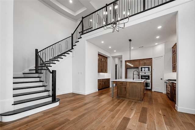 kitchen with a kitchen island with sink, decorative light fixtures, a high ceiling, wood-type flooring, and appliances with stainless steel finishes