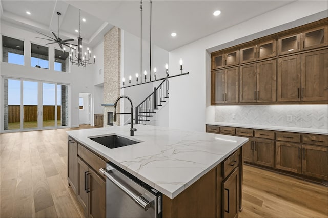 kitchen featuring an island with sink, light stone countertops, sink, dishwasher, and pendant lighting