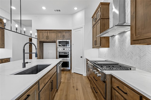 kitchen with appliances with stainless steel finishes, light stone counters, wall chimney range hood, pendant lighting, and sink