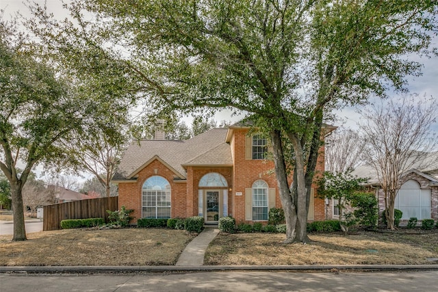 view of front of house featuring brick siding, fence, a chimney, and roof with shingles