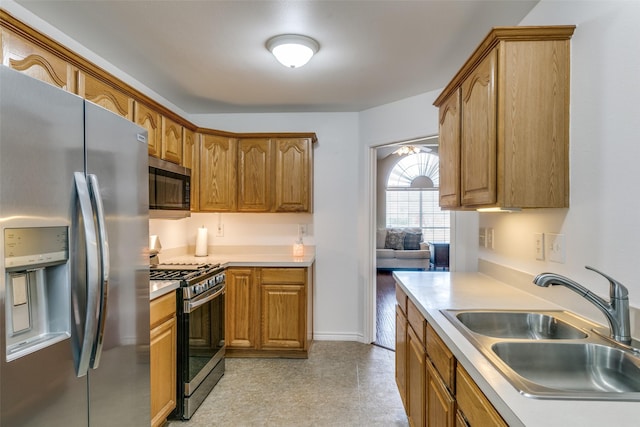 kitchen featuring stainless steel appliances, light countertops, brown cabinetry, a sink, and baseboards