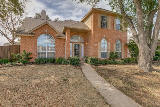 traditional home featuring brick siding, fence, a chimney, and roof with shingles