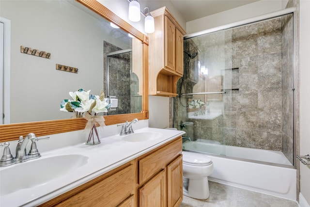 full bath with toilet, double vanity, bath / shower combo with glass door, and a sink