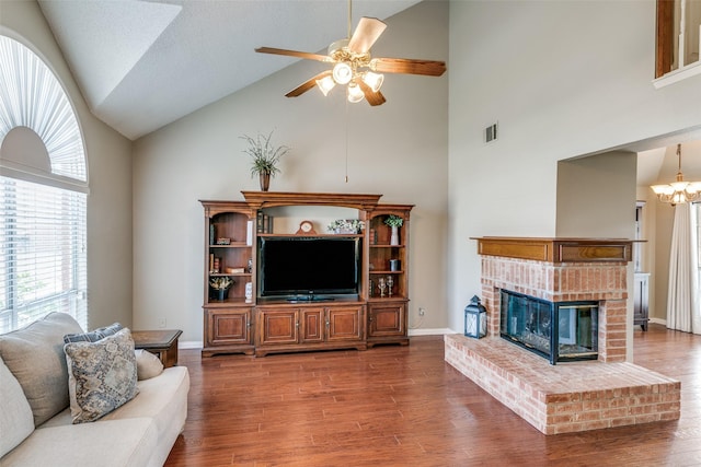 living room featuring a brick fireplace, visible vents, wood finished floors, and ceiling fan with notable chandelier