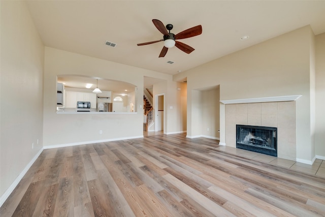 unfurnished living room with a tiled fireplace, ceiling fan, and light wood-type flooring