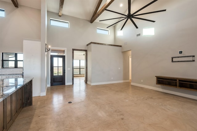 unfurnished living room featuring ceiling fan, beamed ceiling, and a high ceiling