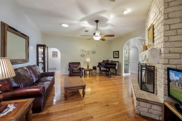 living room featuring a fireplace, ceiling fan, and light wood-type flooring