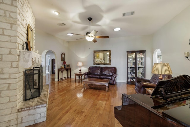 living room with a brick fireplace, ceiling fan, and light wood-type flooring