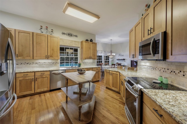 kitchen with sink, decorative light fixtures, stainless steel appliances, and light hardwood / wood-style floors