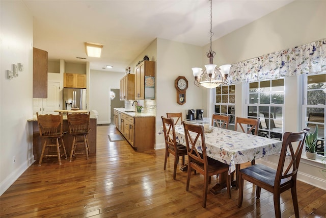 dining space featuring sink, dark wood-type flooring, and an inviting chandelier