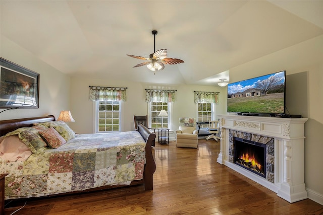 bedroom featuring hardwood / wood-style flooring, multiple windows, vaulted ceiling, and a tile fireplace