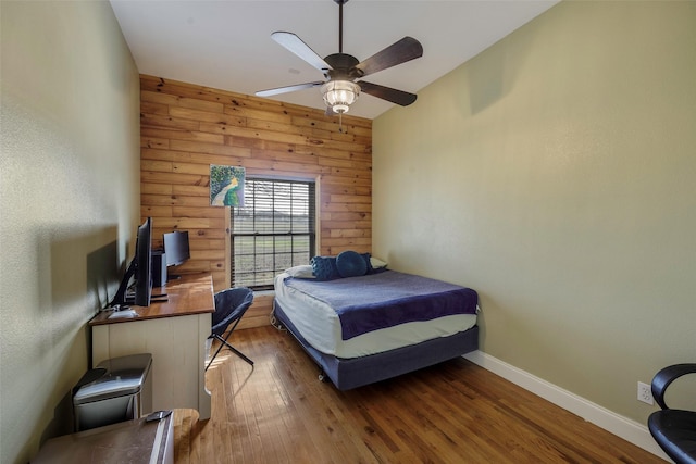 bedroom with ceiling fan, wooden walls, and dark hardwood / wood-style flooring