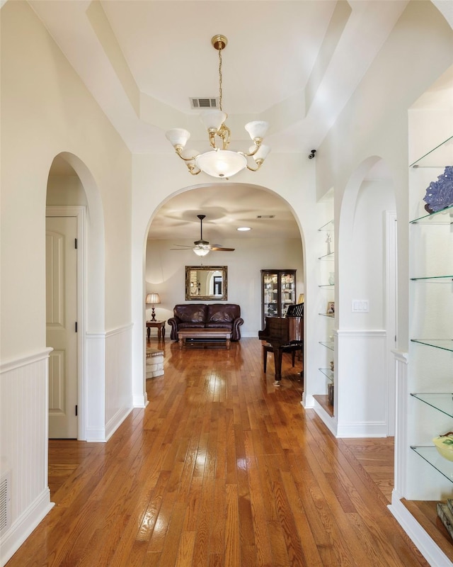 hall with an inviting chandelier, wood-type flooring, a raised ceiling, and built in features