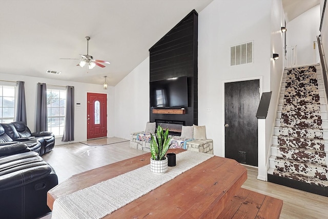 living room featuring ceiling fan, a fireplace, high vaulted ceiling, and light hardwood / wood-style flooring