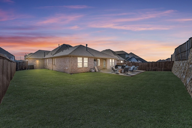 back of property at dusk with a patio area, a fenced backyard, brick siding, and a yard