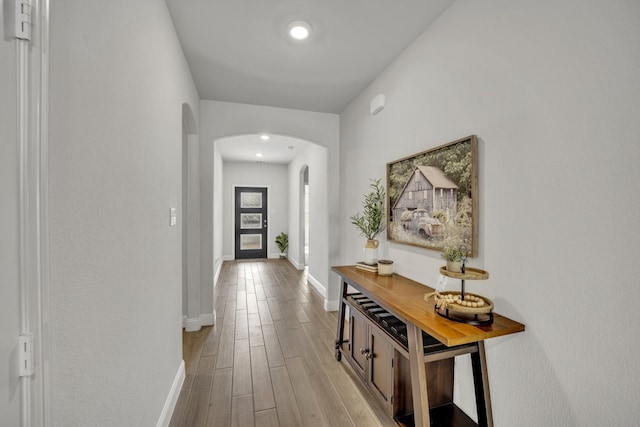 hall with arched walkways, wood finished floors, and baseboards