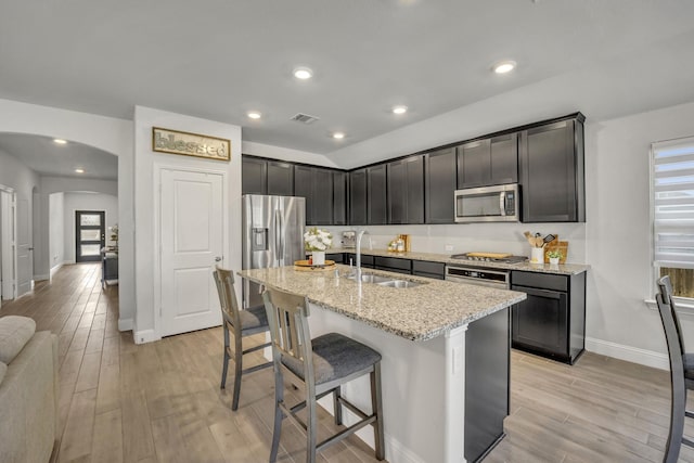 kitchen featuring arched walkways, visible vents, light stone countertops, stainless steel appliances, and a sink