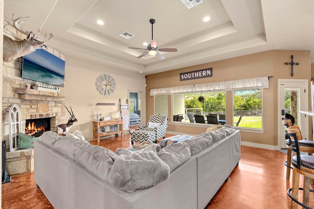 living room featuring a fireplace, a raised ceiling, and ceiling fan