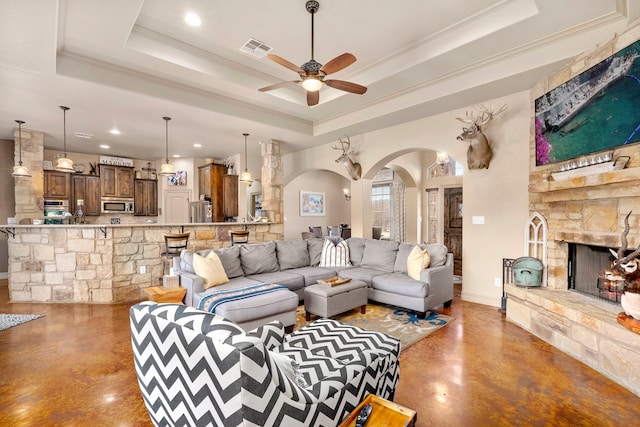 living room featuring a raised ceiling, a stone fireplace, and concrete floors