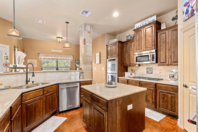 kitchen featuring sink, appliances with stainless steel finishes, backsplash, a kitchen island, and decorative light fixtures