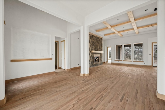 unfurnished living room with wood-type flooring, a stone fireplace, coffered ceiling, and beam ceiling