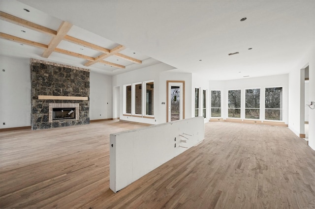 unfurnished living room with beamed ceiling, a fireplace, coffered ceiling, and light hardwood / wood-style flooring