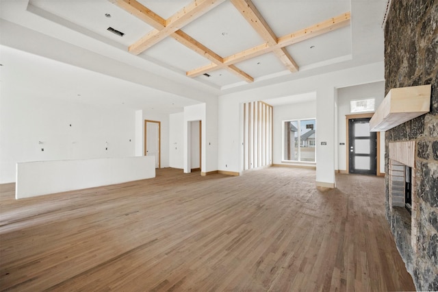 unfurnished living room featuring hardwood / wood-style floors, a towering ceiling, coffered ceiling, a fireplace, and beamed ceiling