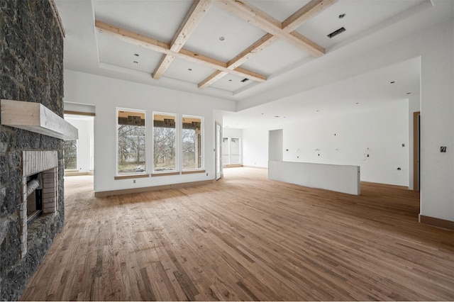 unfurnished living room with a towering ceiling, beamed ceiling, a large fireplace, hardwood / wood-style flooring, and coffered ceiling