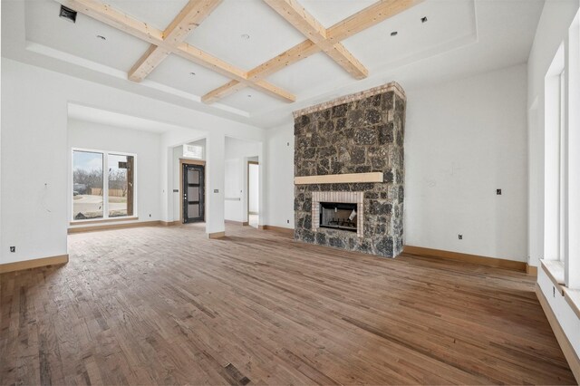 unfurnished living room featuring a towering ceiling, a fireplace, beamed ceiling, hardwood / wood-style flooring, and coffered ceiling