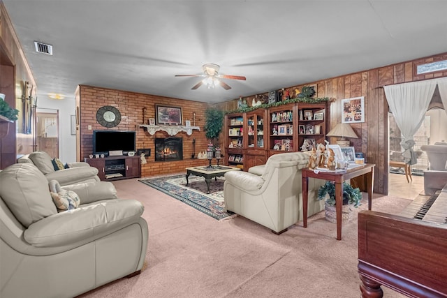 living room featuring a brick fireplace, wooden walls, carpet, and ceiling fan