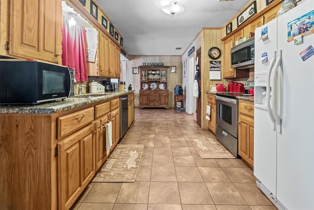 kitchen featuring appliances with stainless steel finishes, sink, dark stone counters, and light tile patterned floors