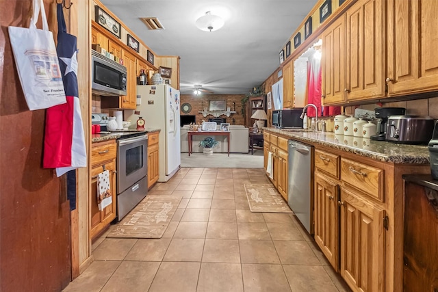 kitchen with light tile patterned flooring, sink, dark stone countertops, appliances with stainless steel finishes, and ceiling fan