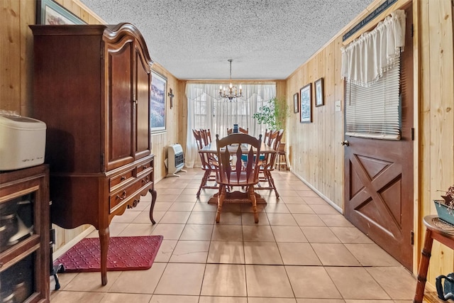 dining area featuring a notable chandelier, wood walls, heating unit, and light tile patterned floors