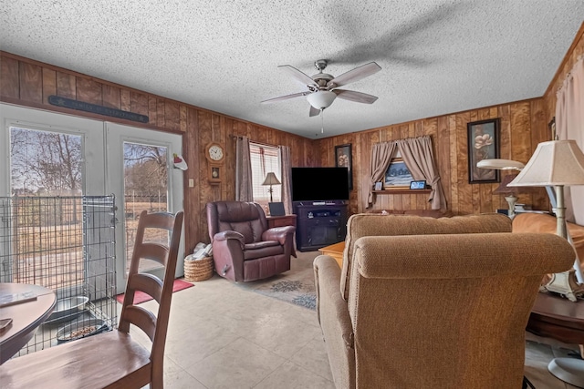 living room featuring wooden walls, a textured ceiling, ceiling fan, and french doors