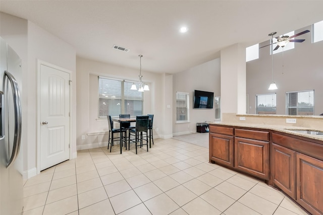 kitchen with ceiling fan with notable chandelier, hanging light fixtures, light tile patterned floors, stainless steel refrigerator with ice dispenser, and light stone countertops