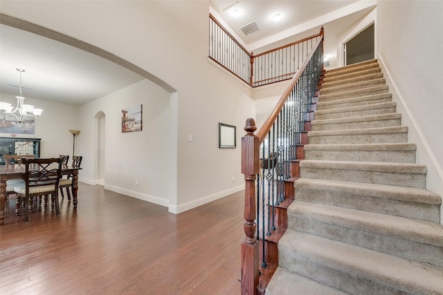 staircase featuring hardwood / wood-style flooring, a towering ceiling, and a chandelier