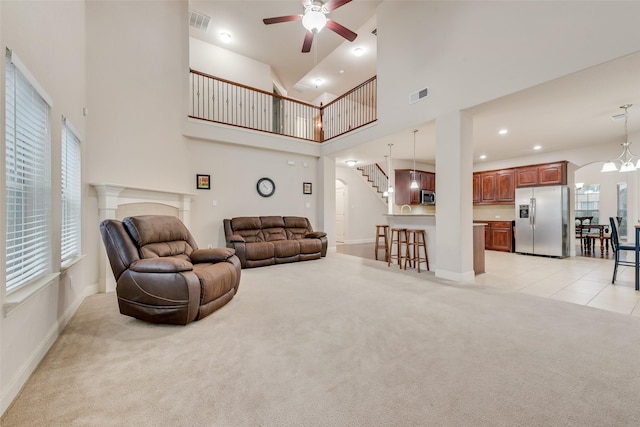 carpeted living room featuring plenty of natural light, ceiling fan with notable chandelier, and a high ceiling