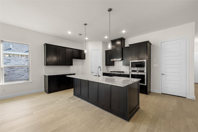 kitchen featuring sink, light stone counters, appliances with stainless steel finishes, an island with sink, and light hardwood / wood-style floors