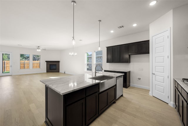 kitchen featuring sink, a kitchen island with sink, stainless steel dishwasher, light stone countertops, and a brick fireplace