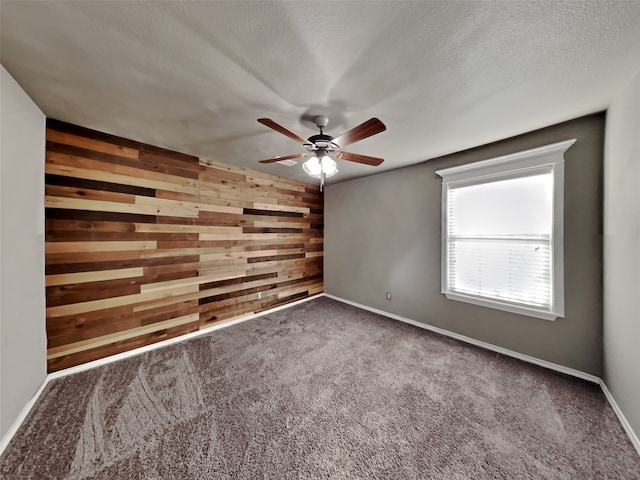 unfurnished room with dark colored carpet, ceiling fan, a textured ceiling, and wooden walls