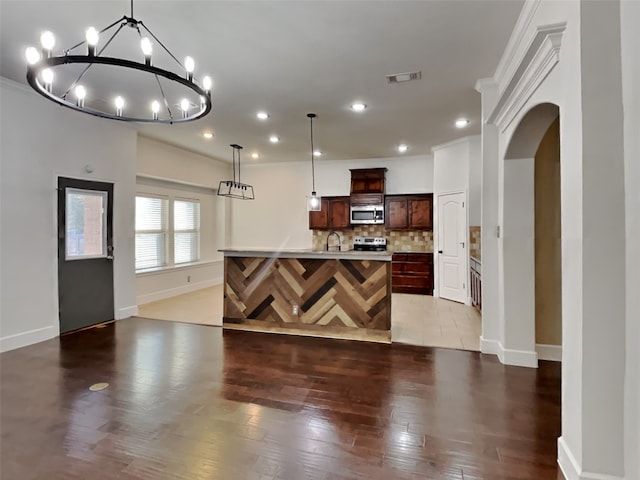 kitchen with appliances with stainless steel finishes, decorative light fixtures, backsplash, dark wood-type flooring, and a center island with sink