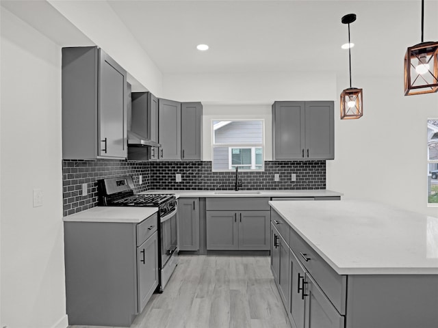 kitchen with gray cabinets, gas stove, hanging light fixtures, and sink