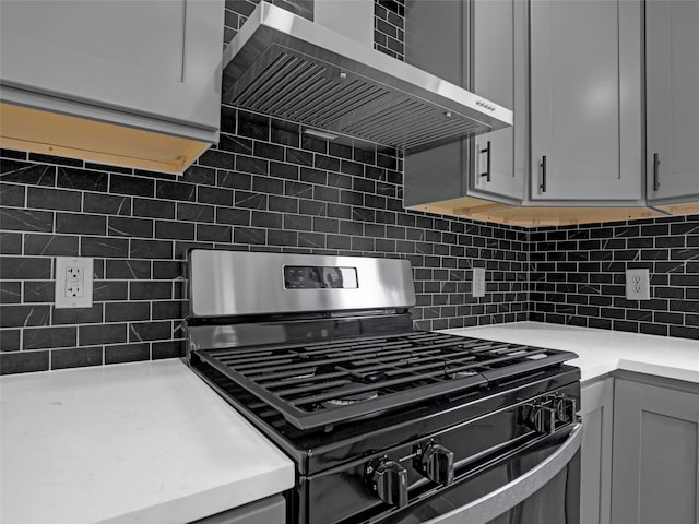 kitchen with backsplash, wall chimney range hood, range with gas stovetop, and gray cabinetry