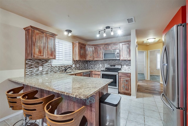 kitchen with appliances with stainless steel finishes, light tile patterned floors, backsplash, and kitchen peninsula