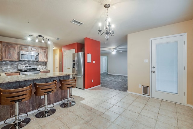 kitchen featuring tasteful backsplash, appliances with stainless steel finishes, kitchen peninsula, pendant lighting, and light stone countertops